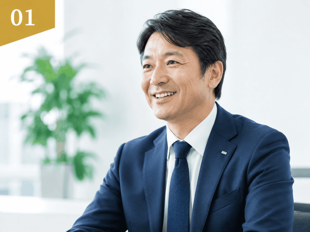 明るいオフィスで微笑むスーツ姿の男性。左上に01のゴールドバナー付き。