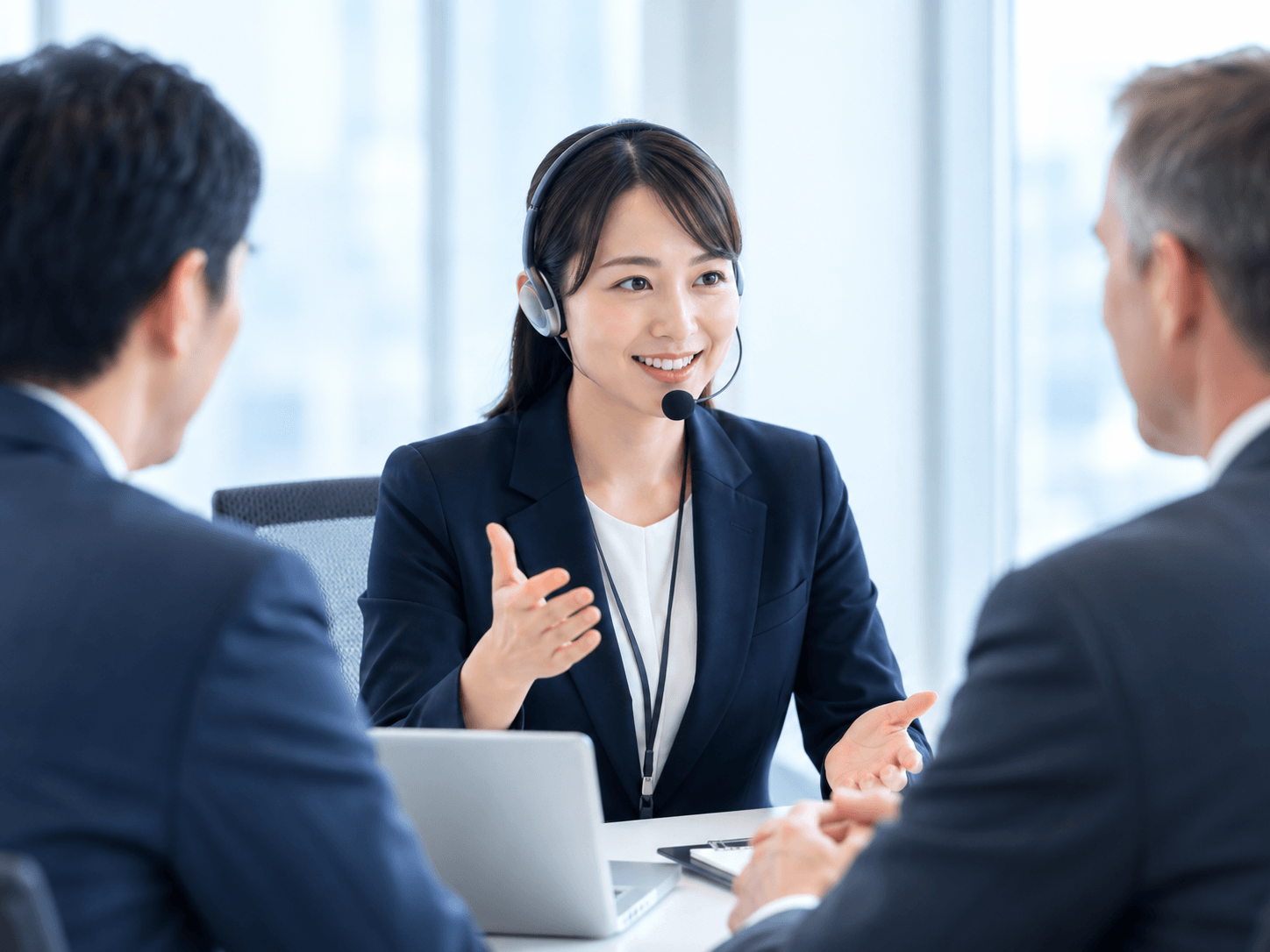 ヘッドセットを着けた通訳者が、向かい合う参加者の会話をサポートする商談風景